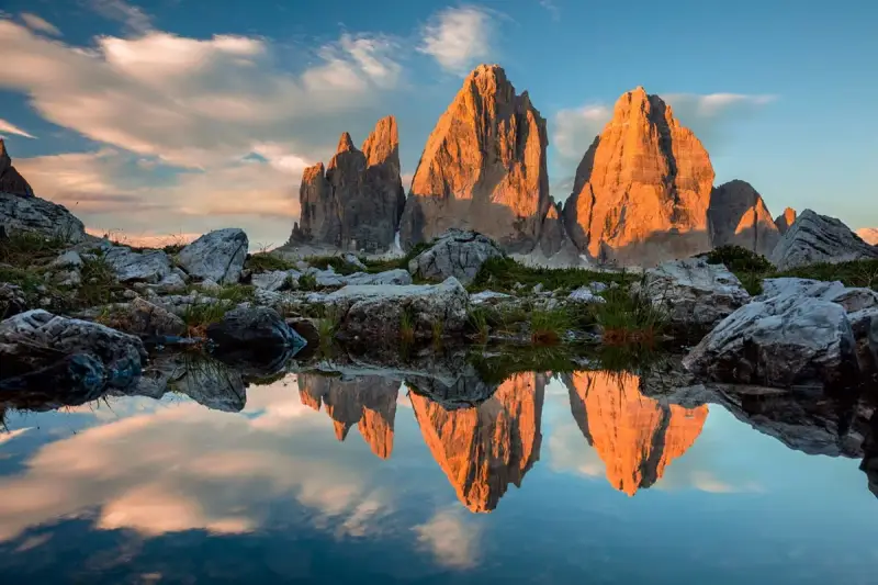 Le Tre Cime di Lavaredo illuminate dal tramonto, riflesse in uno specchio d'acqua. Un paesaggio che incarna la bellezza dei **Dolomiti paesi più belli**.