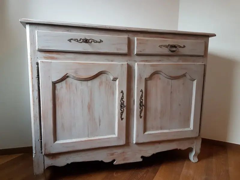 Buffet ancien patiné, avec deux tiroirs et deux portes ornées de poignées en bronze. Le bois présente une finition usée pour un style vintage.