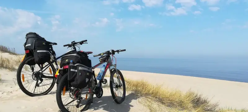 Dwa rowery z sakwami na plaży, gotowe na przygodę wzdłuż Velo Baltica. Morze i niebo tworzą tło.
