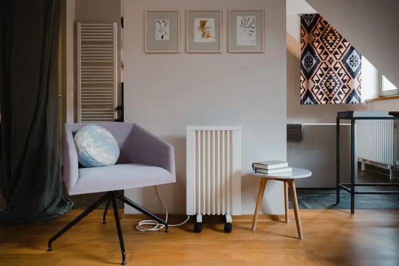 Un fauteuil confortable, un radiateur rayonnant blanc et une petite table avec des livres créent un coin lecture cosy.