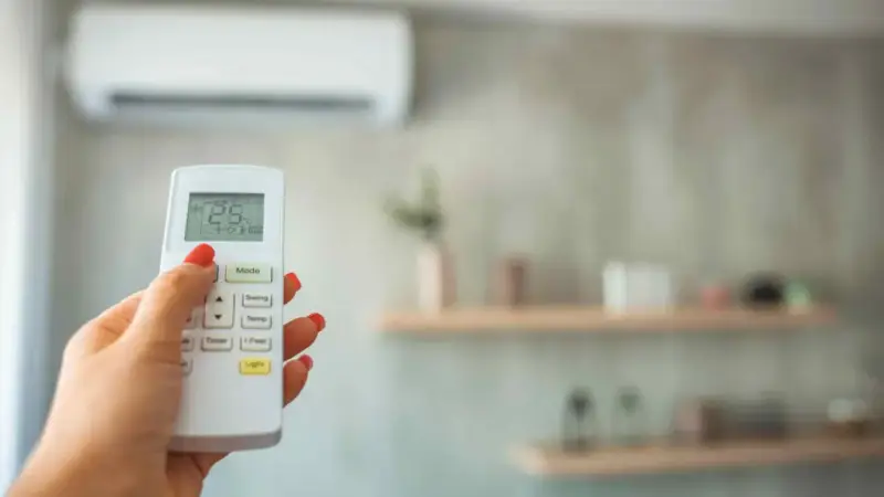 Mano con control remoto ajustando la temperatura ideal aire acondicionado para dormir a 25°C.