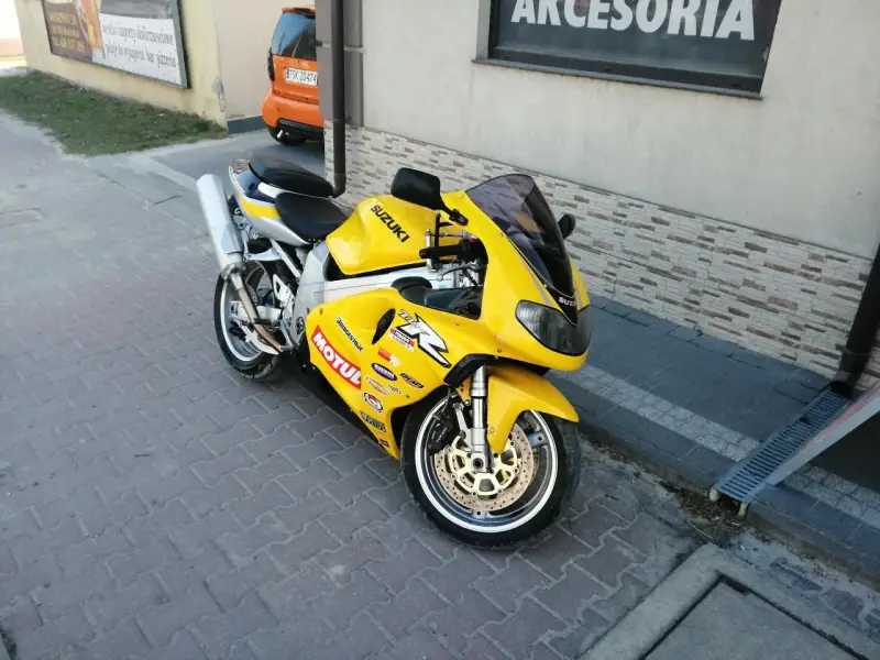 Żółty motocykl Suzuki TL1000R z naklejkami sponsorów, zaparkowany na chodniku.