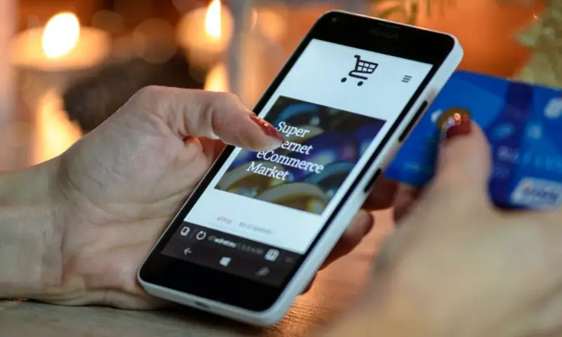 Kobieta z kartą kredytową w dłoni przegląda na smartfonie stronę e-commerce, ucząc się, jak sprzedawać bieliznę w internecie.