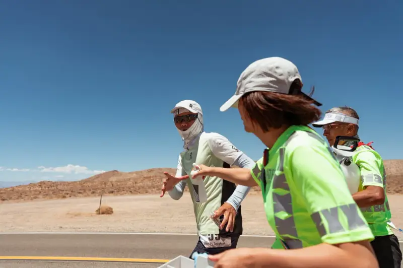 Läufer beim Badwater 135 Ultra-Marathon in der Wüste. Eine Helferin reicht einem Läufer Wasser.
