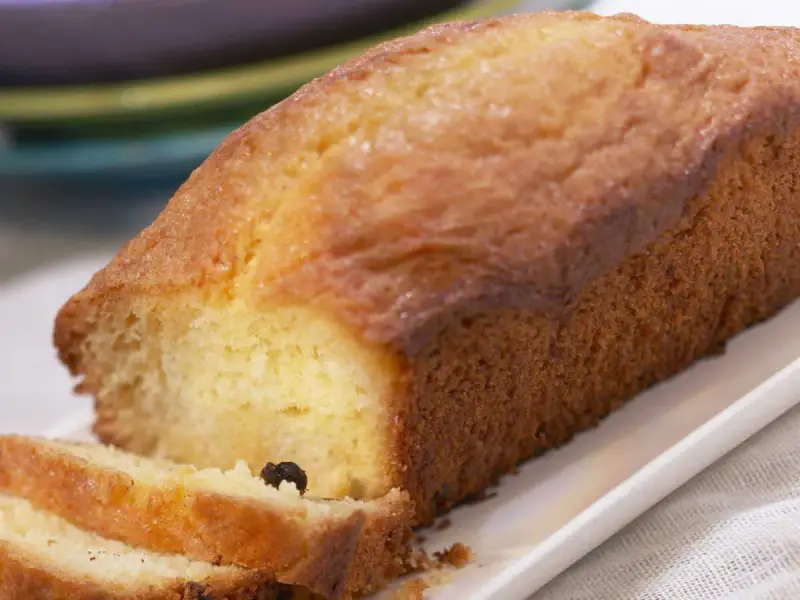 Un cake doré, parfait pour une recette facile. Deux tranches sont coupées, révélant une mie moelleuse et quelques raisins secs.