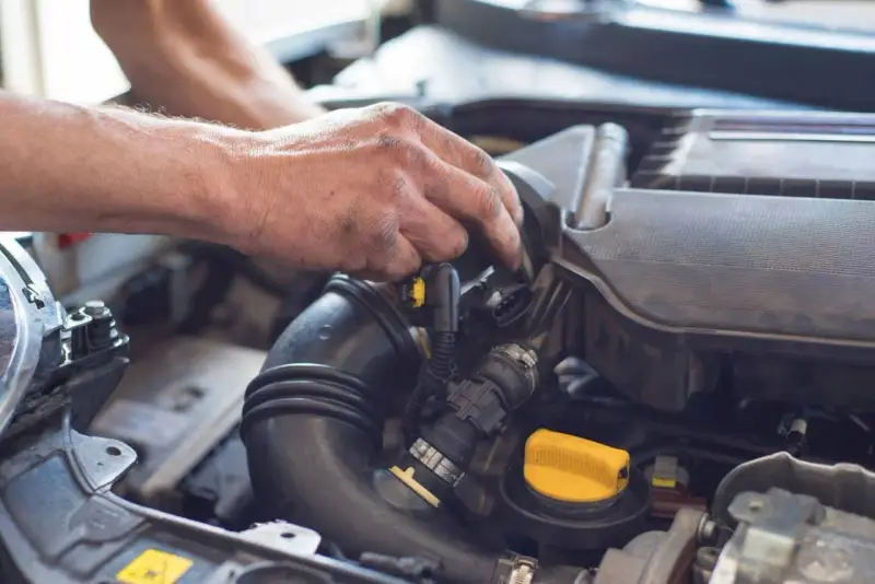 Ręce mechanika pracują przy silniku samochodu. Widoczny jest czarny przewód dolotowy i żółta zakrętka. p0101.