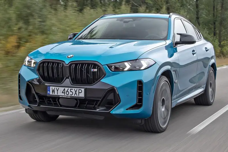 Niebieskie x6 BMW M na drodze, z rozmytym tłem lasu.