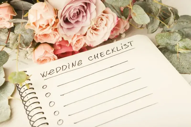 Bukiet róż i eukaliptusa obok notatnika z napisem "Wedding Checklist". Planowanie przebiegu wesela zaczyna się od listy zadań.