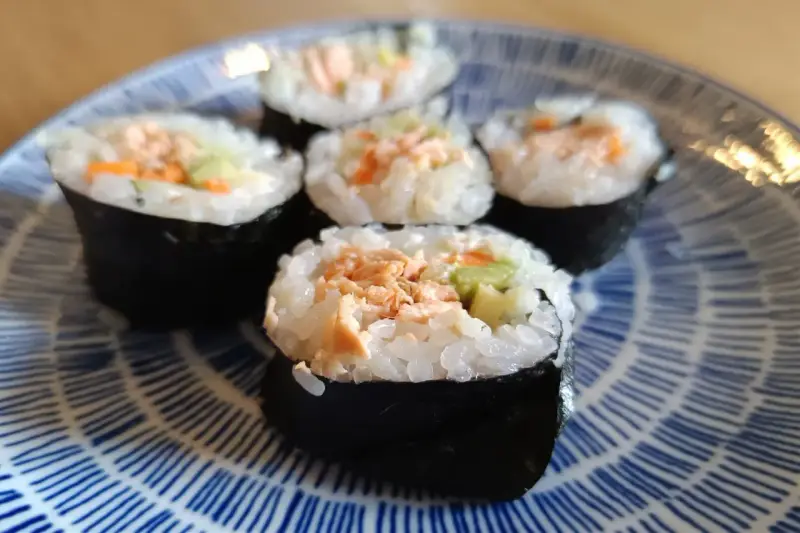Pięć kawałków sushi z łososiem, ryżem i warzywami na niebiesko-białym talerzu.