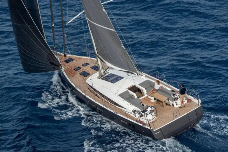 Un couple profite d'une croisière sur un voilier habitable à l'année, naviguant sur des eaux bleues par une journée ensoleillée.