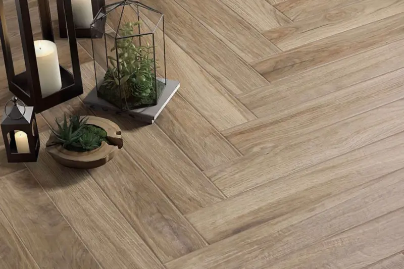 Detalles de cómo colocar azulejos en espiga, con velas y plantas decorativas sobre el suelo de madera.
