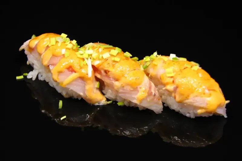 Trzy kawałki sushi z rybą i kremowym sosem, posypane szczypiorkiem. Idealne na lekki posiłek, gdy zastanawiasz się nad sushi kalorie.