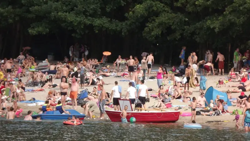 Tłum ludzi odpoczywa na plaży nad jeziorem w Jelczu Laskowicach. Słońce, piasek i woda tworzą idealne warunki do letniego relaksu.