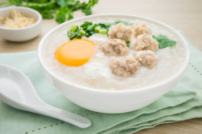 Miseczka pysznego congee z mięsnymi klopsikami, jajkiem i szczypiorkiem. Idealne na rozgrzewający posiłek.