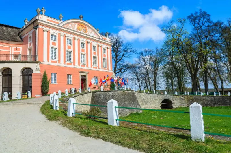 Pałac w Kurozwękach, z flagami narodowymi przed wejściem, zaprasza do odkrywania jego atrakcji.