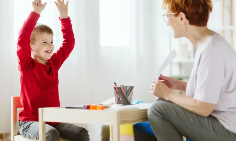 Chłopiec z podniesionymi rękami, uśmiechnięty, podczas sesji terapeutycznej. Może to być pomocne w ocenie objawów ADHD u dzieci test.