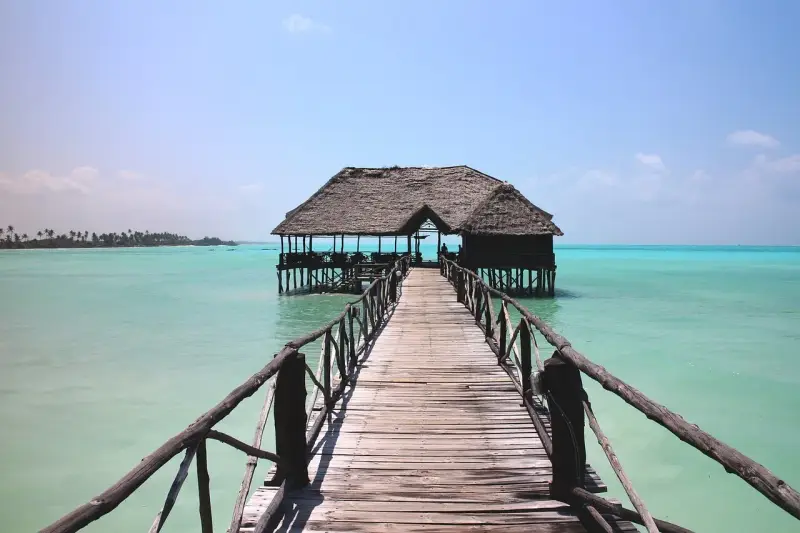 Drewniany pomost prowadzi do chatki na palach na turkusowej wodzie. Idealne miejsce na wiza zanzibar.