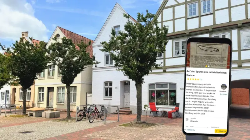 Blick auf die mittelalterliche Itzehoe Altstadt mit Fachwerkhäusern und einem Smartphone, das Informationen über die Stadt anzeigt.
