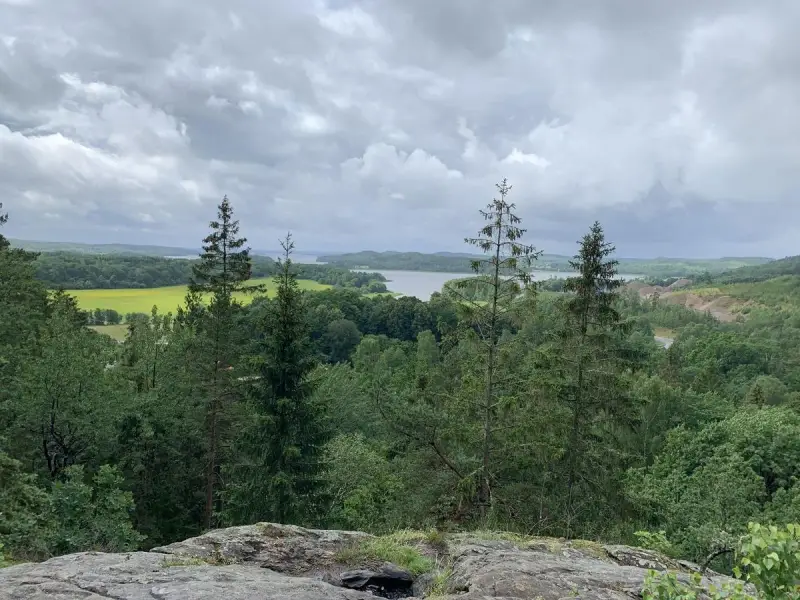 Vacker utsikt över sjö och skog, perfekt för vandringsleder Alingsås. Molnig himmel över det gröna landskapet.
