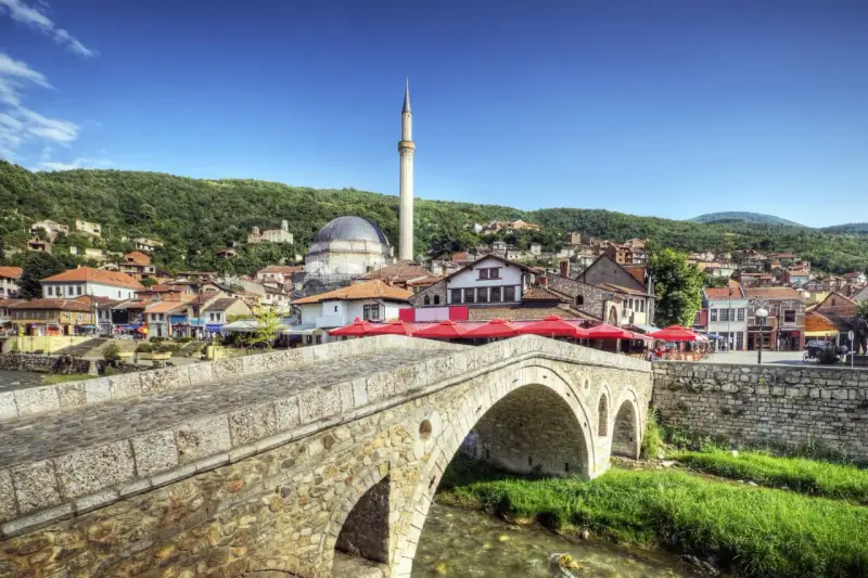 Kamienny most nad rzeką, z widokiem na meczet i miasto na wzgórzu. Kosowo atrakcje turystyczne zachwycają.