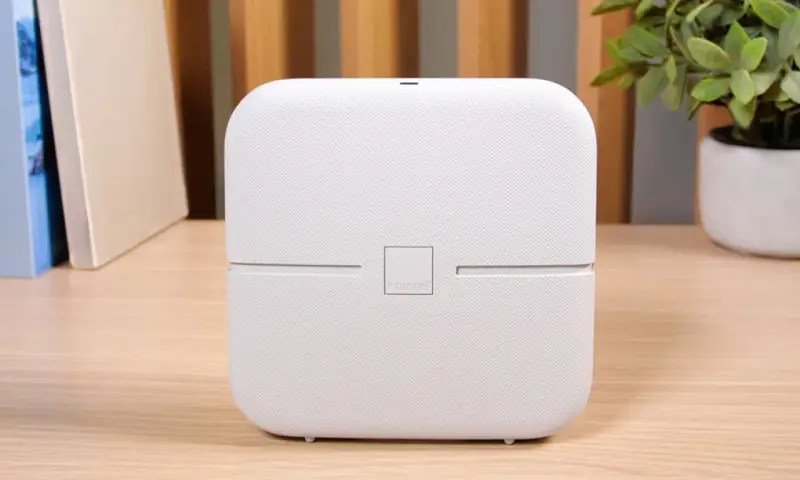 Biały router funbox 7 Orange, z logo operatora, stoi na drewnianym biurku obok książek i rośliny.