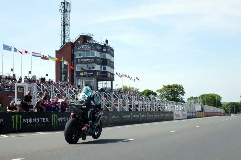 Motocyklista ściga się na wyspie Man, mijając trybuny pełne widzów i wieżę kontrolną.