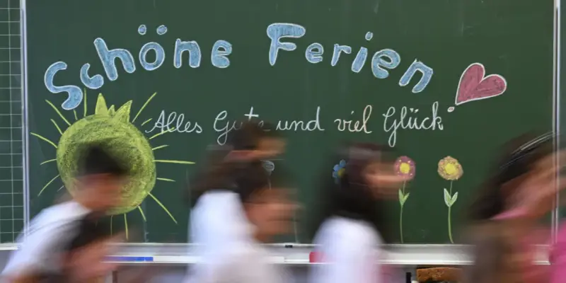 Kreidetafel mit "Schöne Ferien" und einem lachenden Smiley, bereit für die herbstferien 2025 nrw. Kinder huschen vorbei.