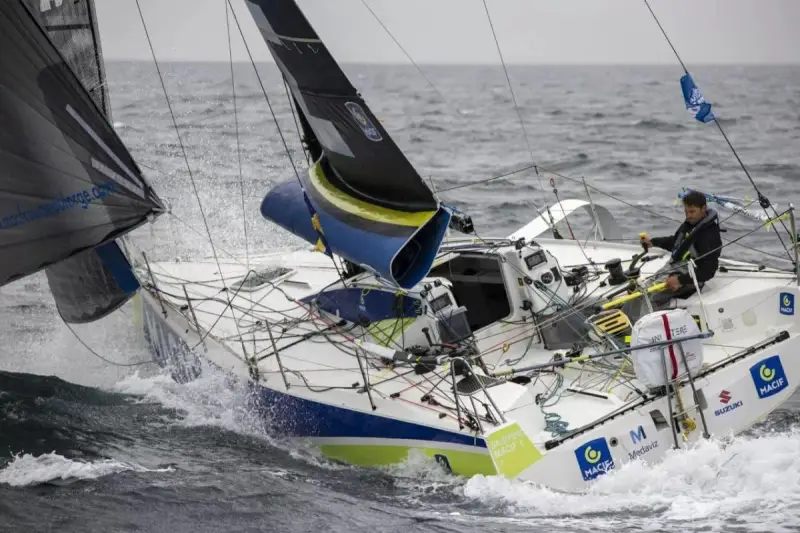 Un skipper navigue sur un voilier blanc et bleu, affrontant les vagues. Le nom "Pierre Quiroga" est visible sur la coque.
