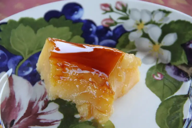 Un trozo de tocino de cielo de la abuela, con su caramelo brillante, sobre un plato decorado con flores y frutos.