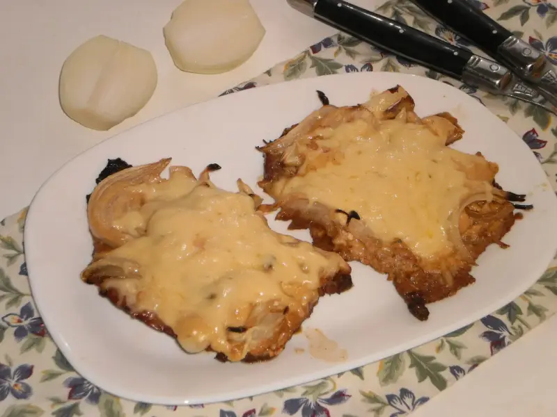 Pyszny schab w cebuli, zapieczony z serem, idealny na niedzielny obiad. Obok leżą połówki cebuli.