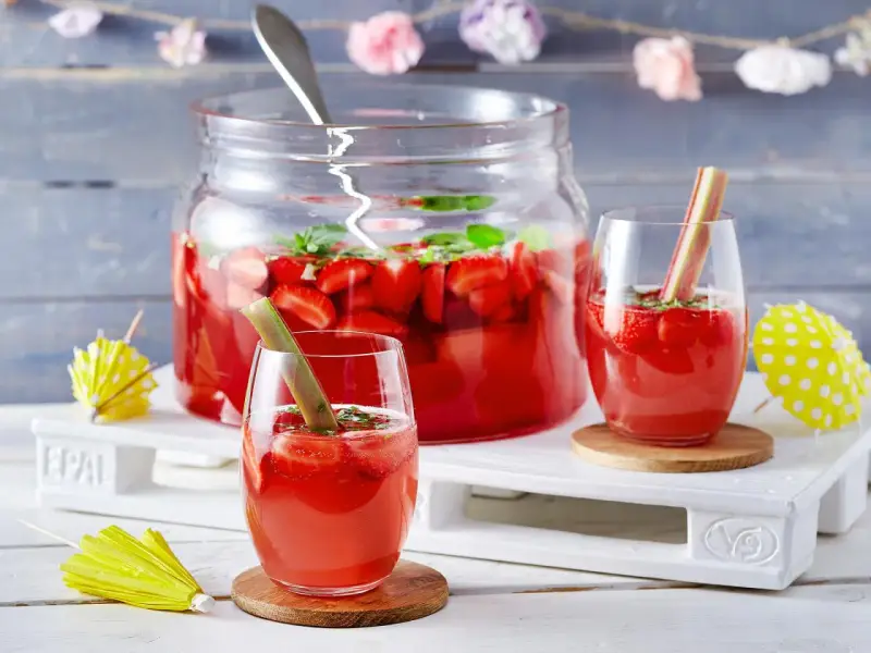 Erfrischende Rhabarber Bowle mit Erdbeeren und Minze, garniert mit Rhabarberstücken. Perfekt für den Sommer!