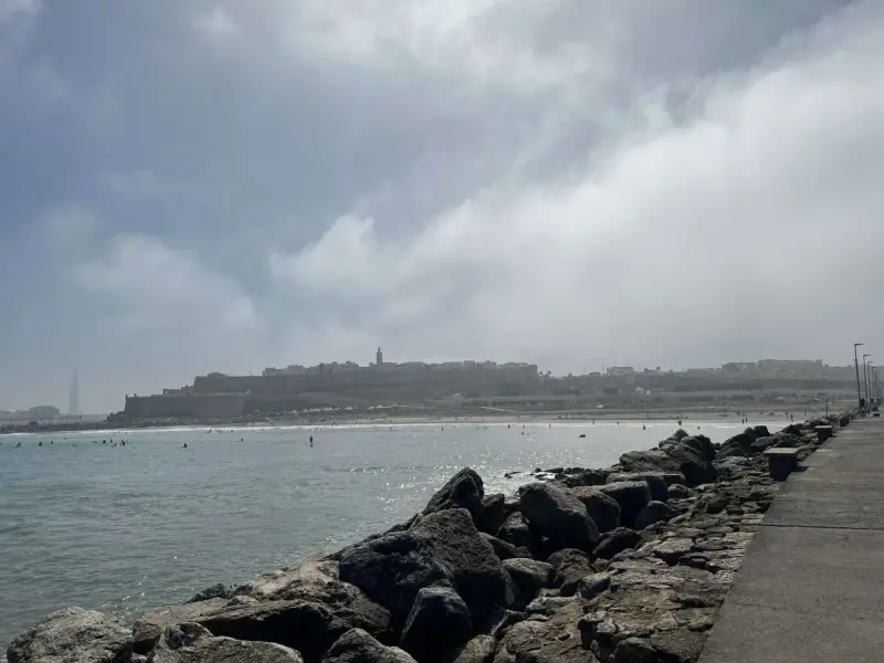 Spokojna plaża z surferami i miastem w tle. Czy Maroko jest bezpiecznym krajem? Widok sugeruje, że tak, ludzie cieszą się słońcem i morzem.