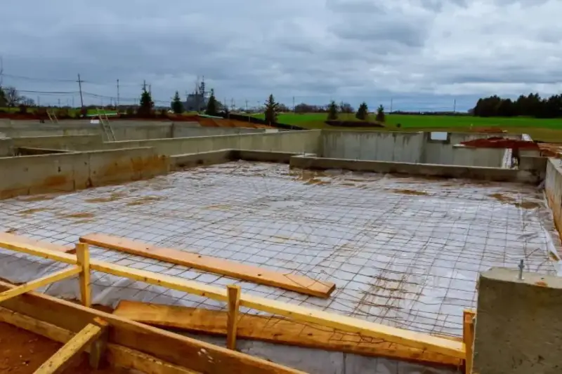 Fundament budowlany z zbrojeniem, przygotowany pod wylanie betonu. Widać betonowe ściany fundamentowe i siatkę stalową na podłożu.