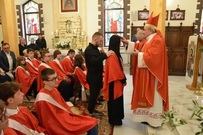 Biskup udziela sakramentu bierzmowania. Ceremonia, choć uroczysta, nie trwa długo. Młodzi ludzie w czerwonych szatach czekają na swoją kolej.