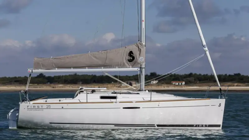 Voilier blanc "First 25 Performance" naviguant sur une mer calme, avec une voile grise arborant un logo noir.