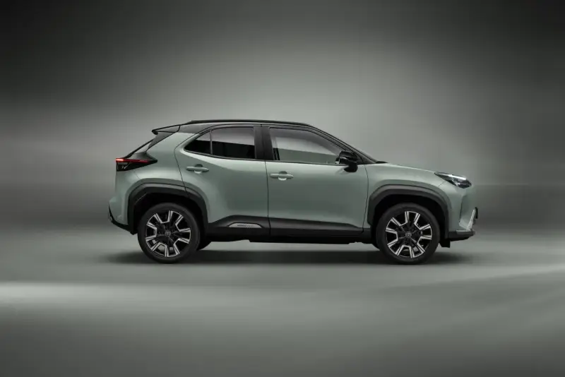Nowy, zielony toyota crossover Yaris Cross z czarnym dachem i felgami stoi na szarym tle.
