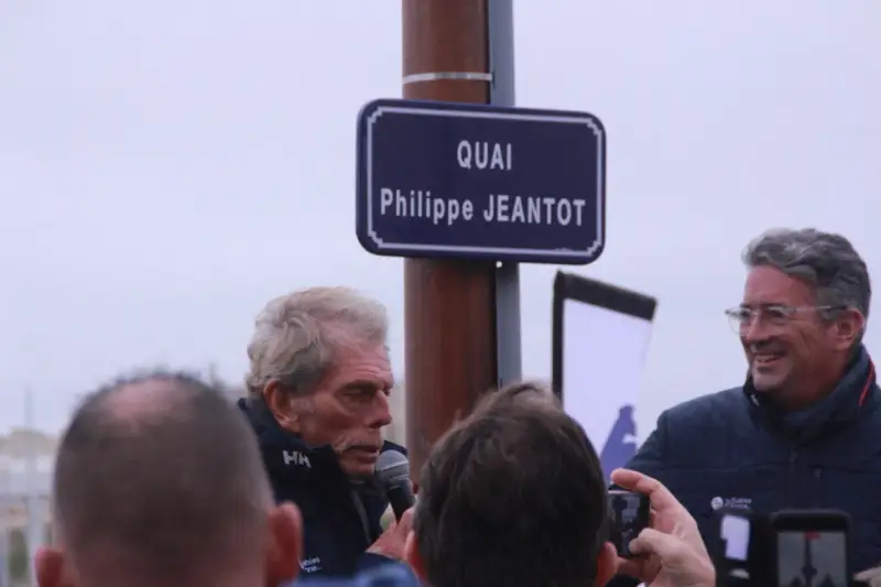 Un panneau "Quai Philippe JEANTOT" honore le navigateur. Philippe JEANTOT, entouré, parle au micro.