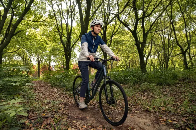 Mężczyzna w kasku jedzie rowerem trekkingowym po leśnej ścieżce. Taki rower to wszechstronny towarzysz podróży.