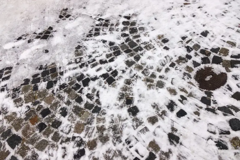 Zimowa kostka brukowa pokryta śniegiem i śladami opon. Zastanawiasz się, czym posypać kostkę brukową zimą, by była bezpieczna?