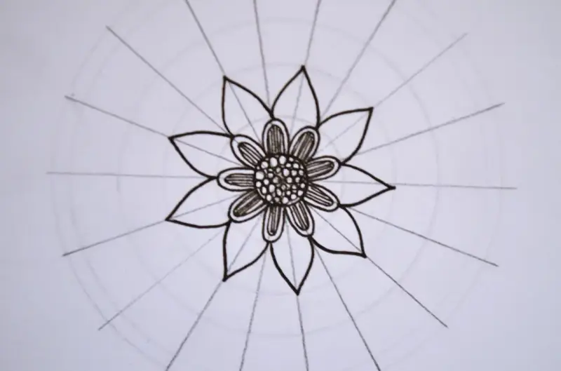 Kwiatowa mandala, rysowana czarnym tuszem, z delikatnymi okręgami i promieniami.