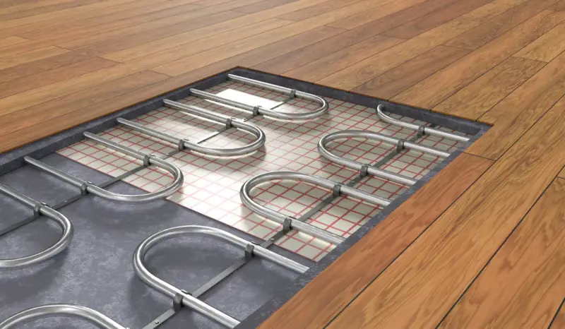 Système de chauffage au sol interdit, avec tuyaux métalliques courbés sur une grille isolante sous un plancher en bois.