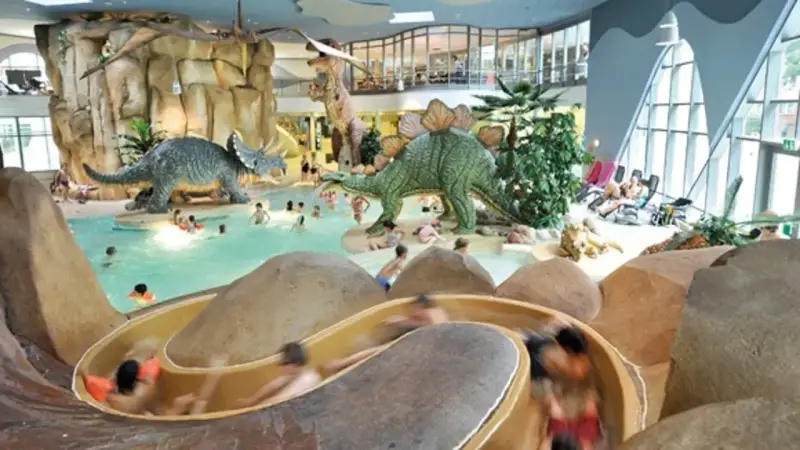 Kinder planschen im Dino-Bad, ein perfektes Ziel für die Herbstferien in Hamburg. Rutschen und Dinosaurier sorgen für Spaß.