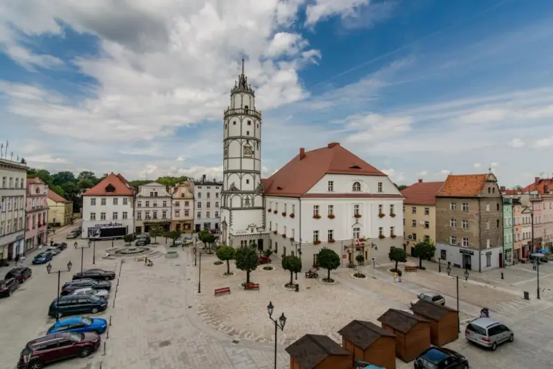Rynek w Paczkowie, polskie Carcassonne, z ratuszem i wieżą. Brukowany plac, samochody, ławki i małe drewniane budki.