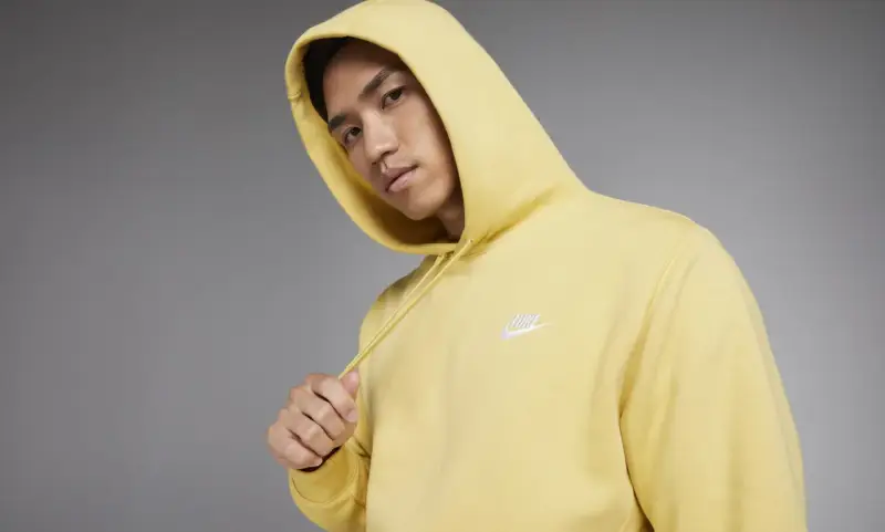 Młody mężczyzna w żółtej bluzie z kapturem Nike Club.