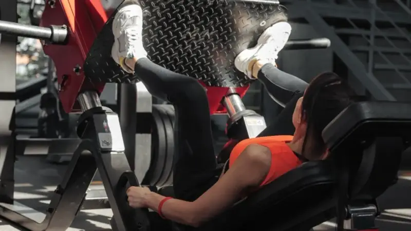 Kobieta ćwiczy na maszynie do wyciskania nóg, wykonując ćwiczenie push pull legs.