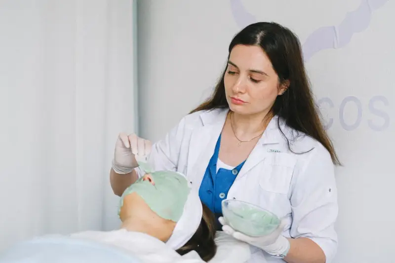 Dermatolog nakłada zieloną maskę na twarz pacjentki.