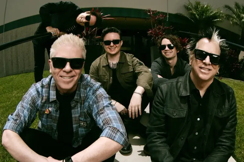 Les membres de The Offspring posent ensemble, souriants et portant des lunettes de soleil. Le groupe semble prêt pour une nouvelle aventure musicale.