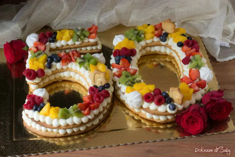 Torta 50 anni con panna, frutta fresca e biscotti a forma di numero. Un dolce colorato e delizioso per festeggiare un traguardo importante.