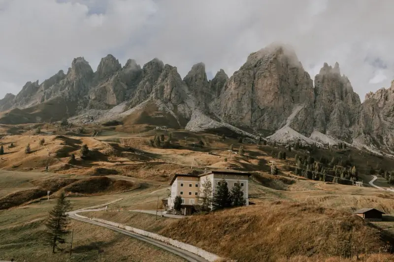 Malownicze **Val di Funes** z górami w tle, hotel na wzgórzu i kręta droga.