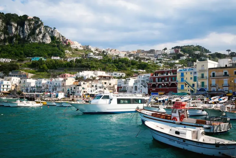 Barche nel porto di Capri, con la città arroccata sulla collina. Un ottimo punto di partenza per capire come raggiungere Capri da Napoli.